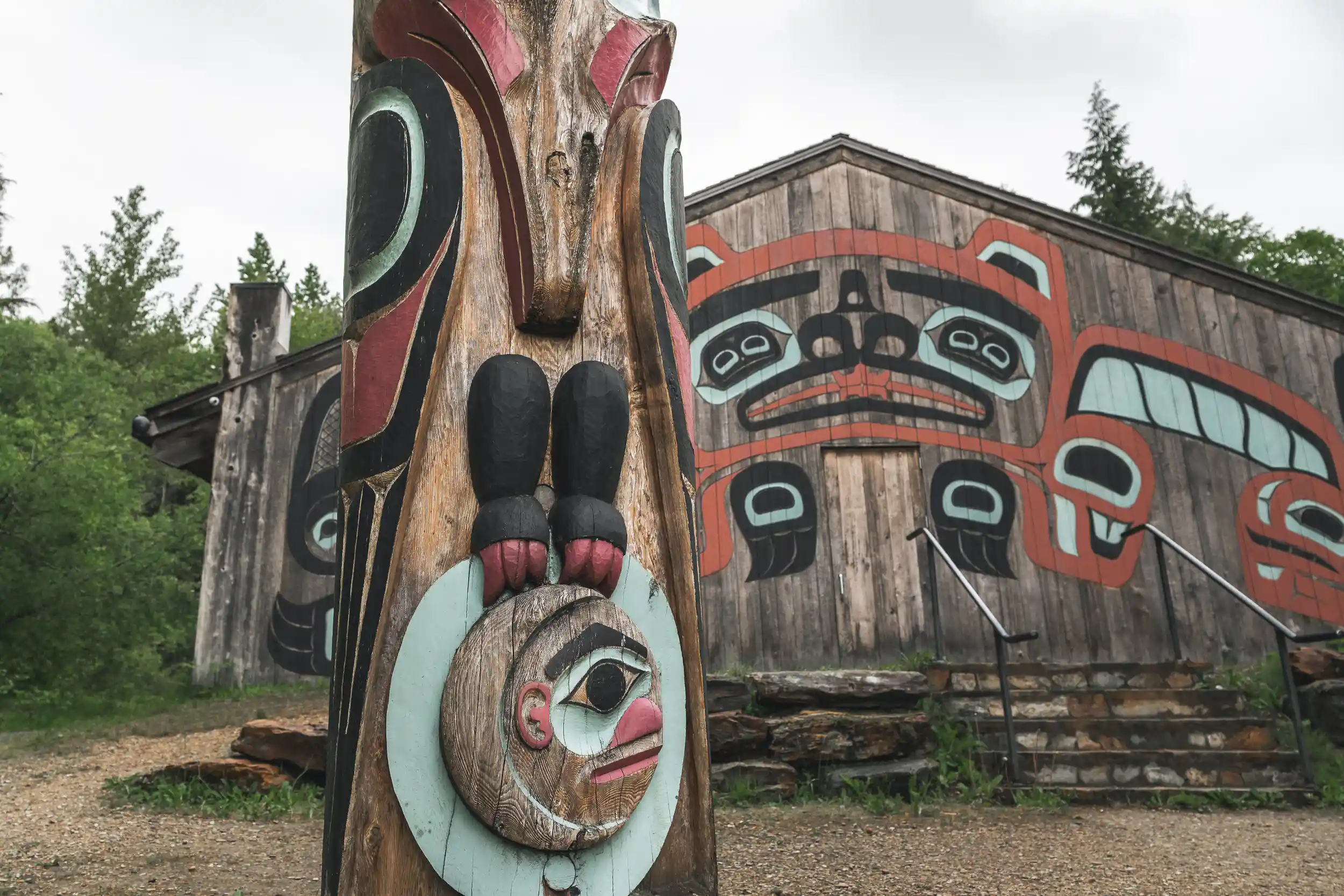 Carved totem pole in front of a painted clan house at Saxman Native Village near Ketchikan, Alaska