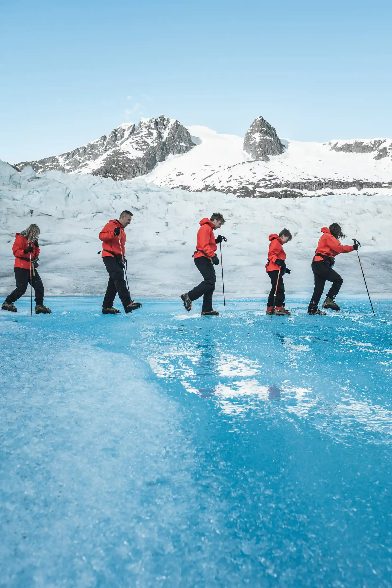Five glacier trekkers in red jackets crossing blue ice on Mendenhall Glacier