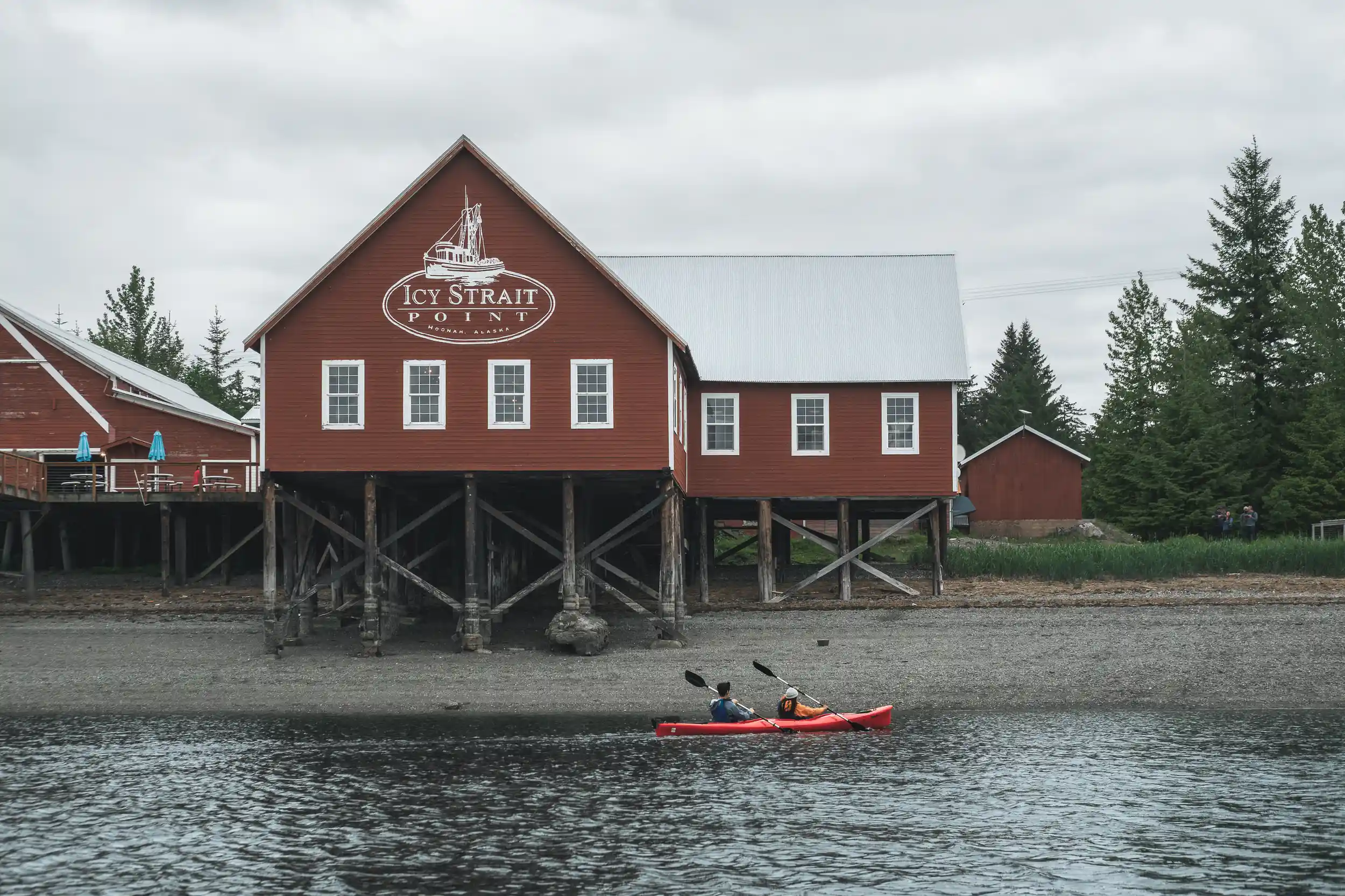 Tandem kayak paddling past the red cannery building at Icy Strait Point in Hoonah, Alaska