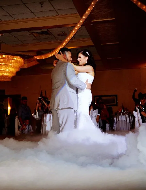 Bride and groom dancing closely on a cloud-like fog during their wedding reception with guests watching.