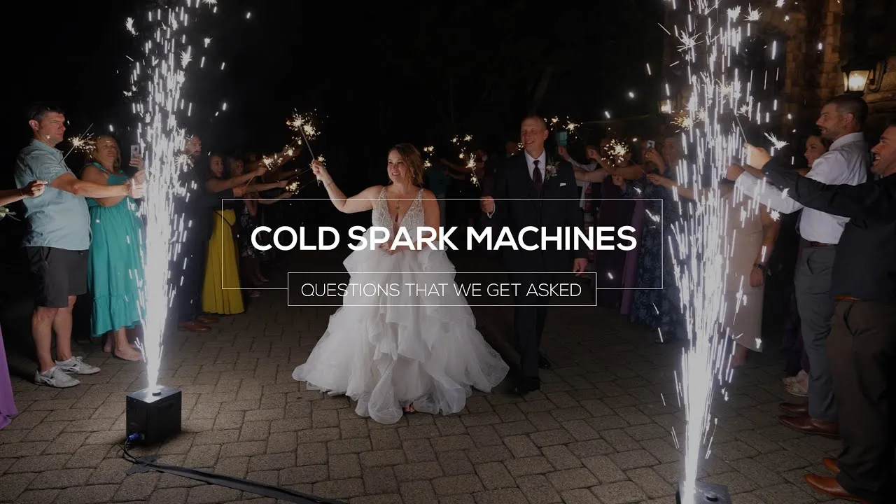 Bride and groom walking between crowds holding sparklers, with cold spark machines shooting sparks on both sides at night.