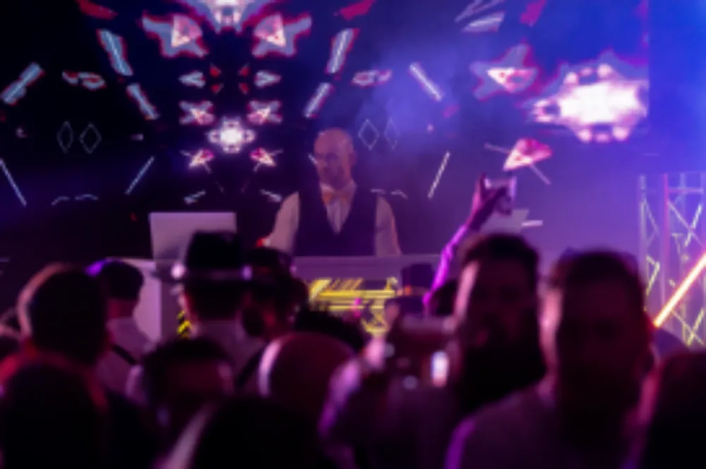 DJ performing on stage with colorful lights and a crowd dancing in front.