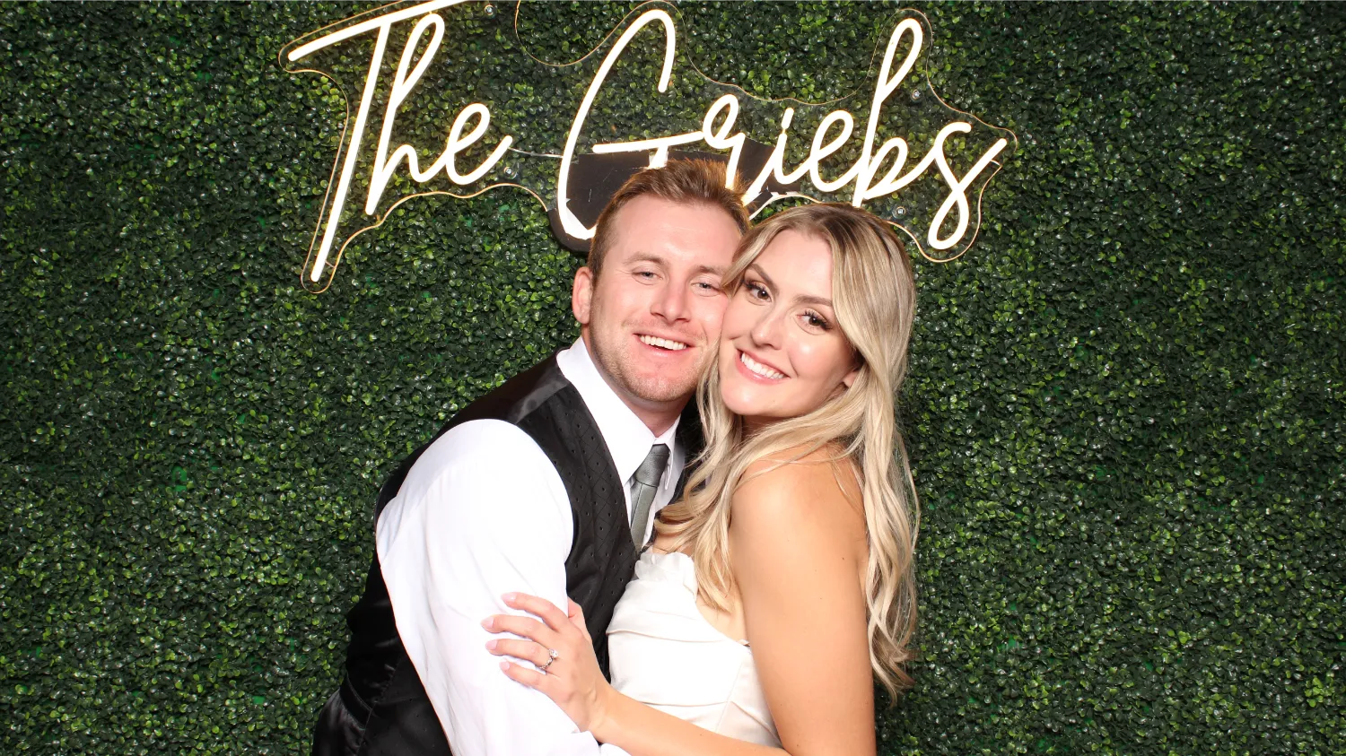 A man and woman pose for a picture in front of a sign that says The Greibes.