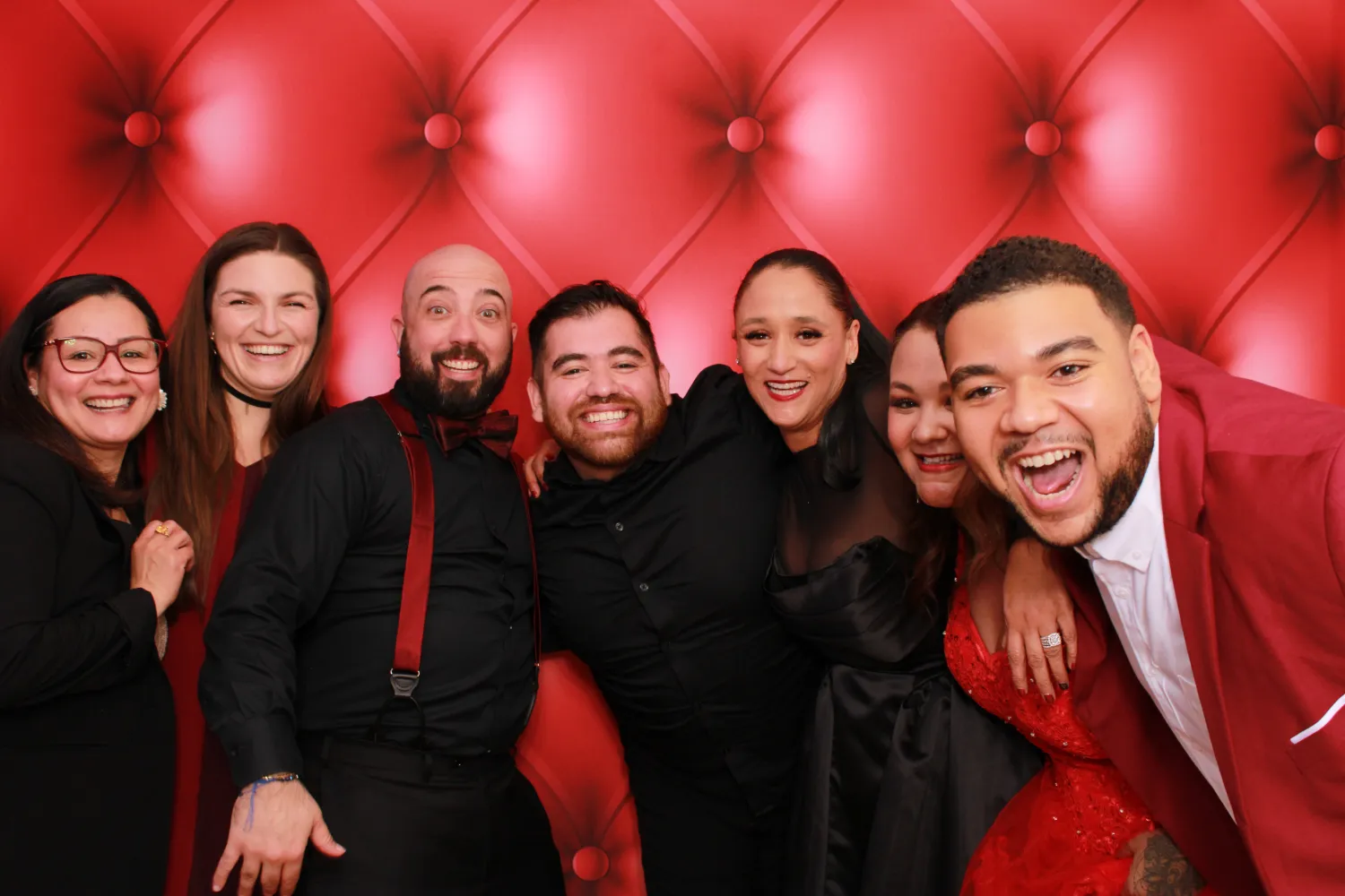 Group of friends smiling together in front of red tufted background