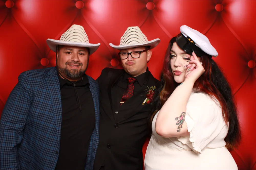 Three people posing in cowboy hats and stylish attire against red background