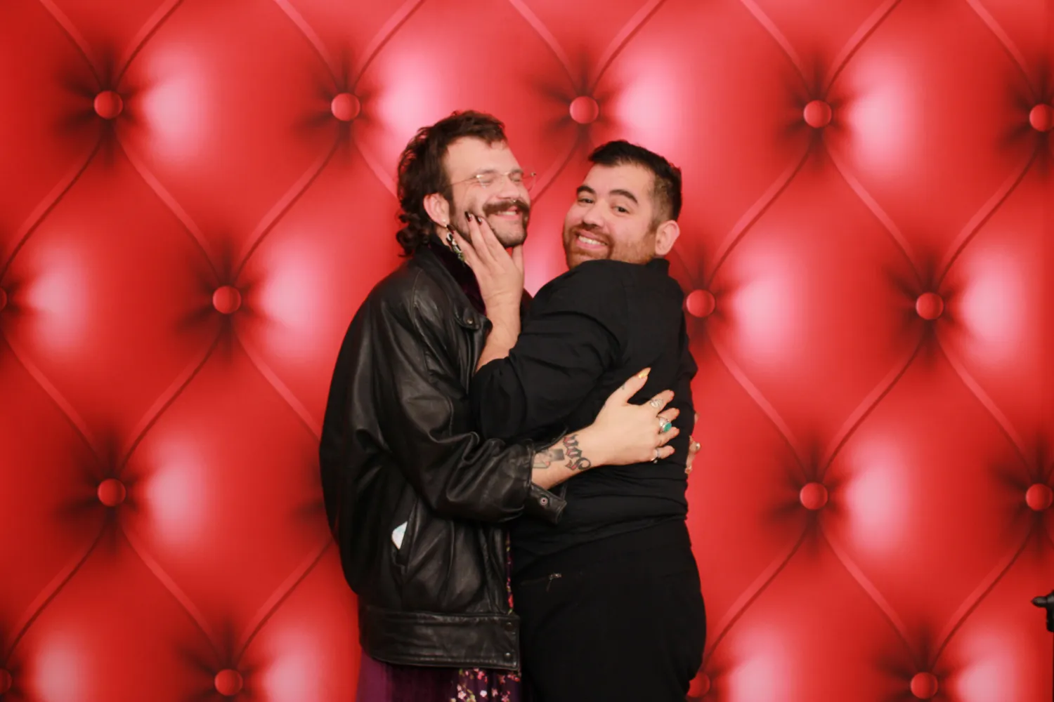 Two people hugging and smiling against a red tufted background