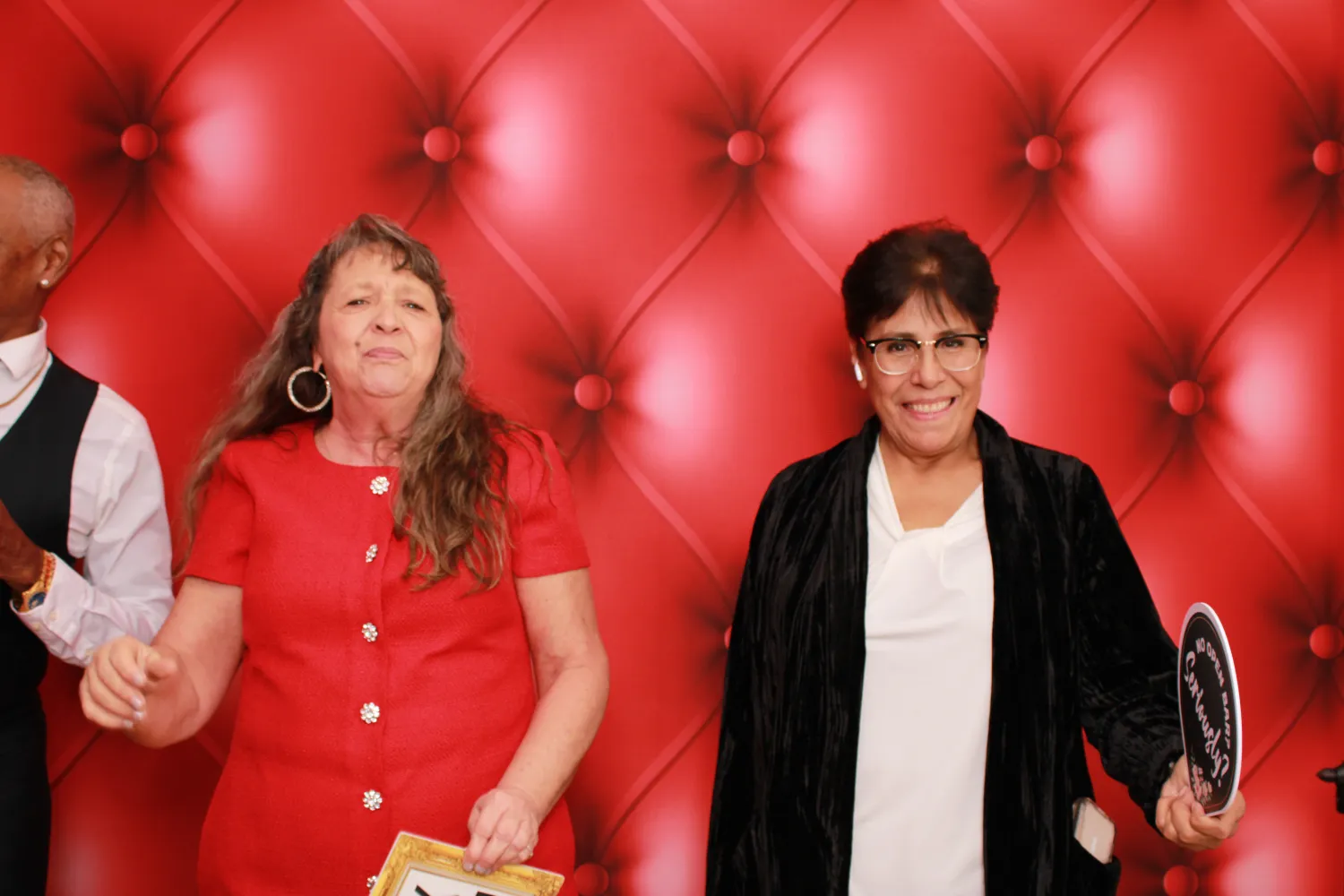 Two women standing in front of a red tufted background, smiling