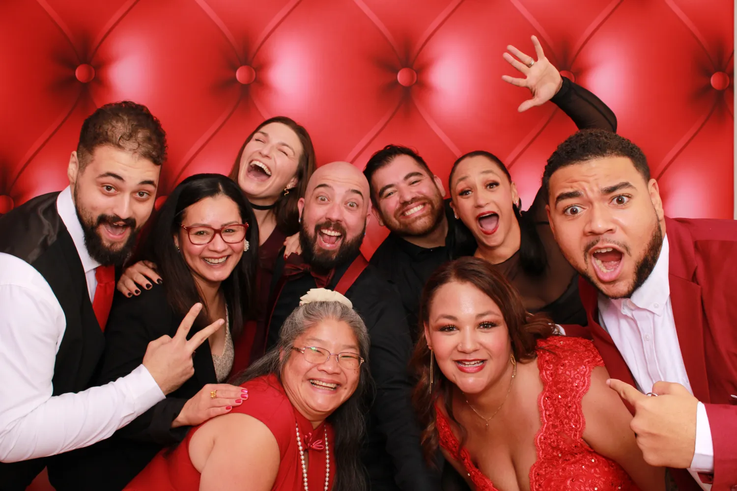 Large group of people laughing and posing together against red background