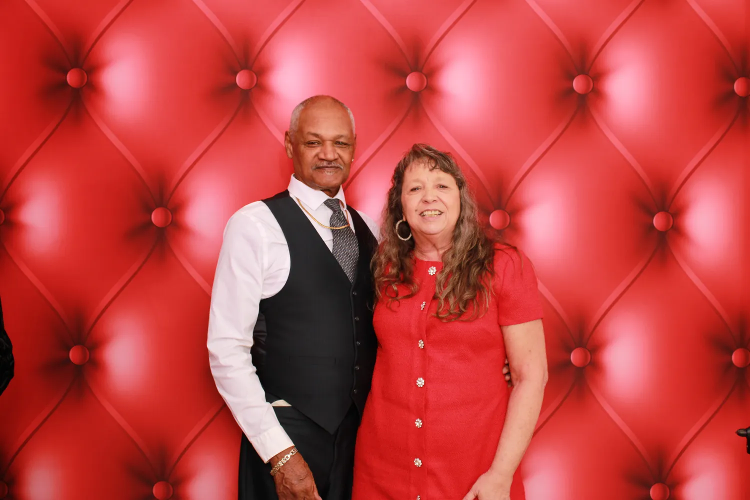 Mature couple posing together in front of plush red tufted backdrop