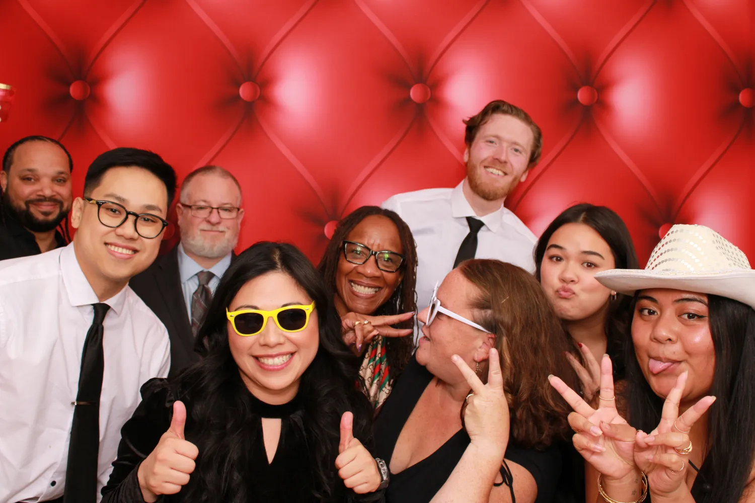 Diverse group of coworkers posing together with fun gestures against red backdrop