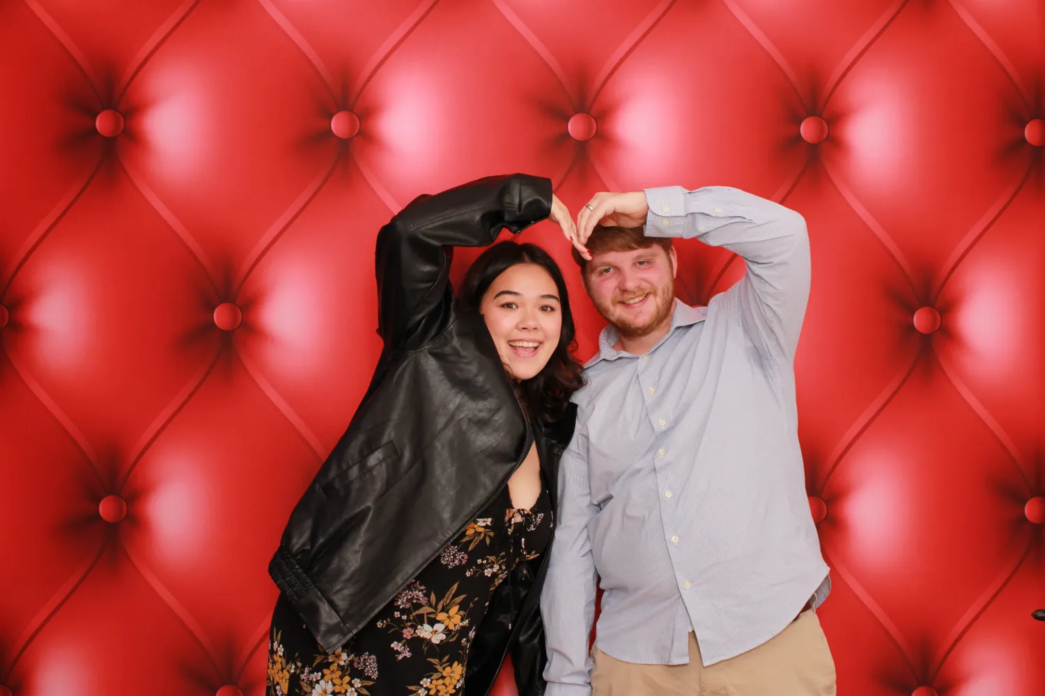 Two people making heart shape against red tufted backdrop