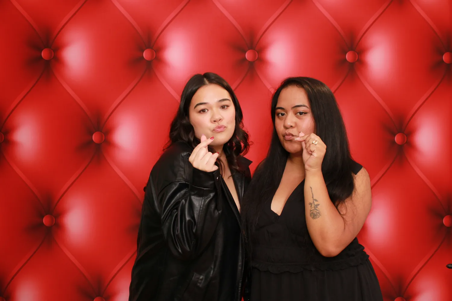 Two friends posing playfully against a red tufted leather backdrop
