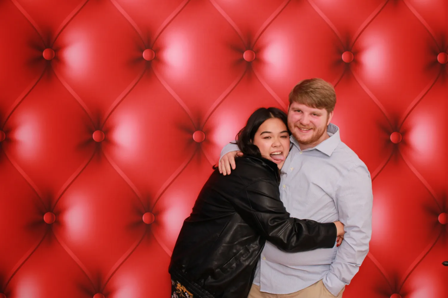 Couple hugging and laughing in front of a red tufted background