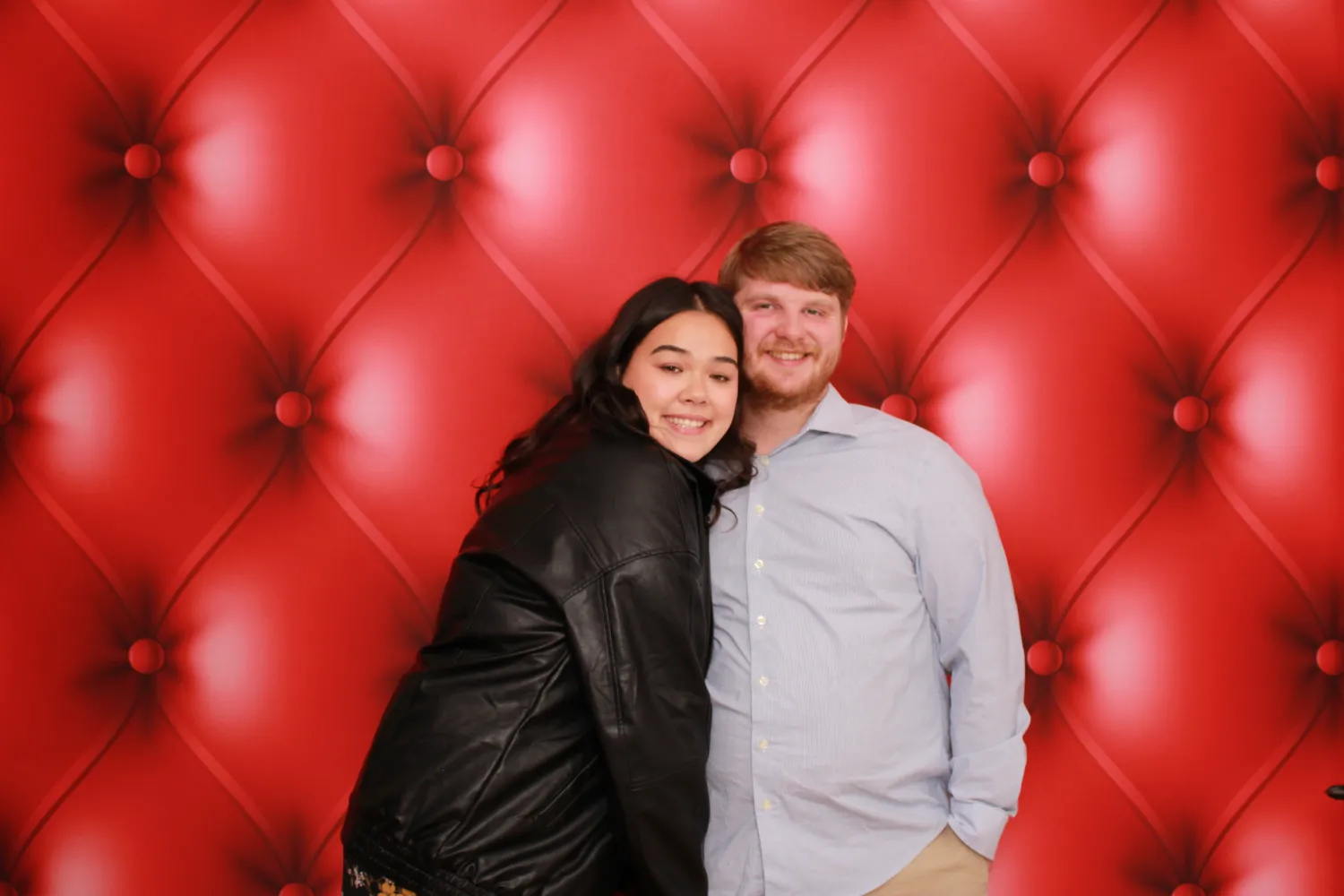Couple smiling together against a plush red tufted background