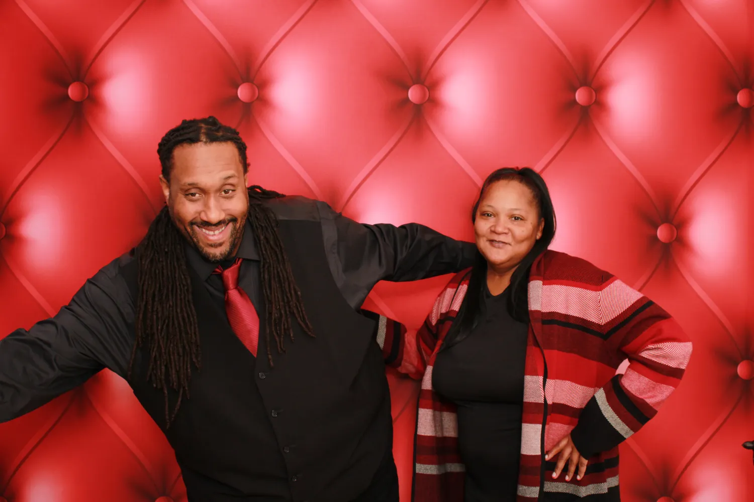 Two people posing together against a red tufted background, smiling