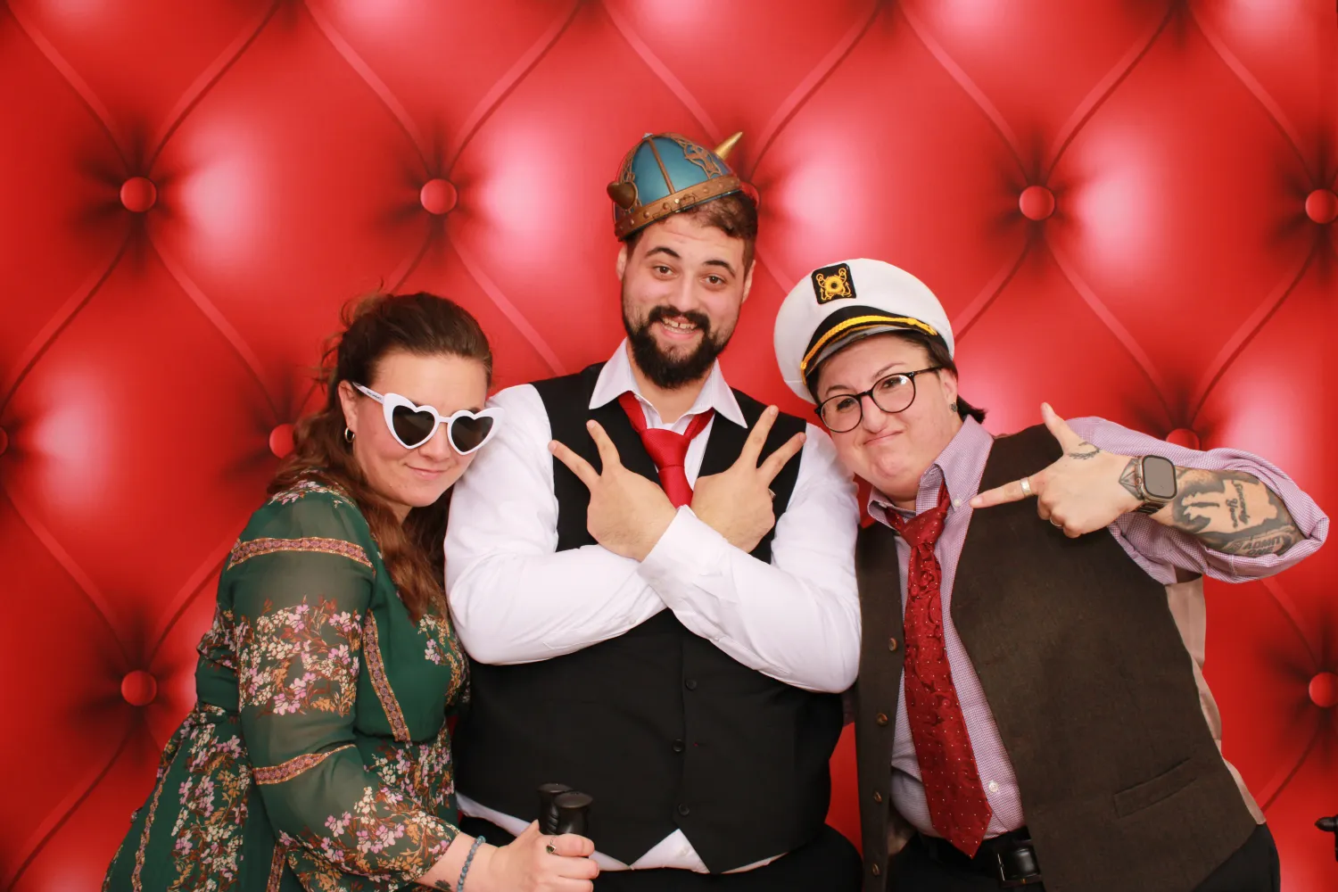Three people posing in fun costumes against red tufted background