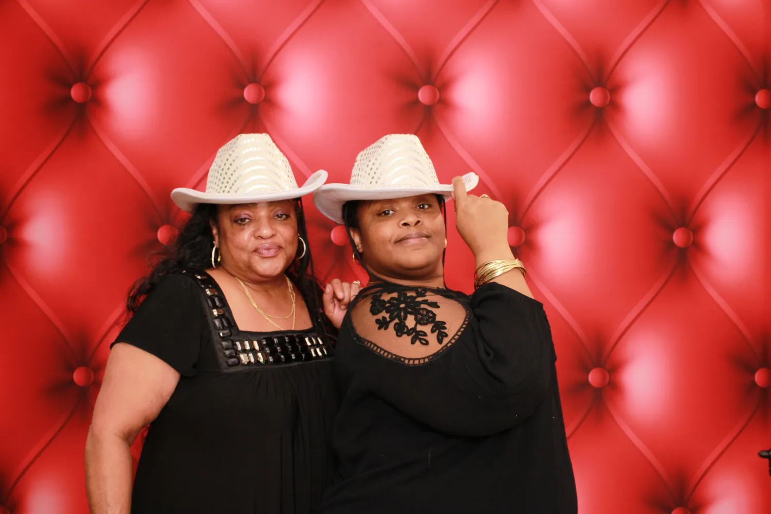 Two women in black outfits and white cowboy hats pose against red background
