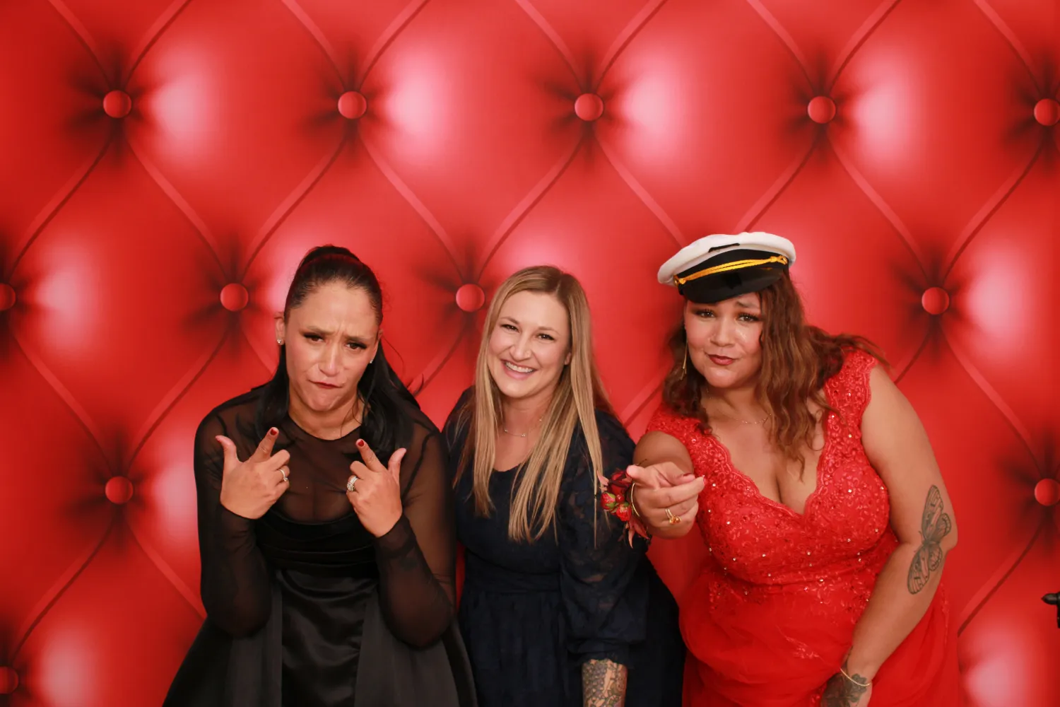 Three women posing in front of red tufted backdrop with different expressions