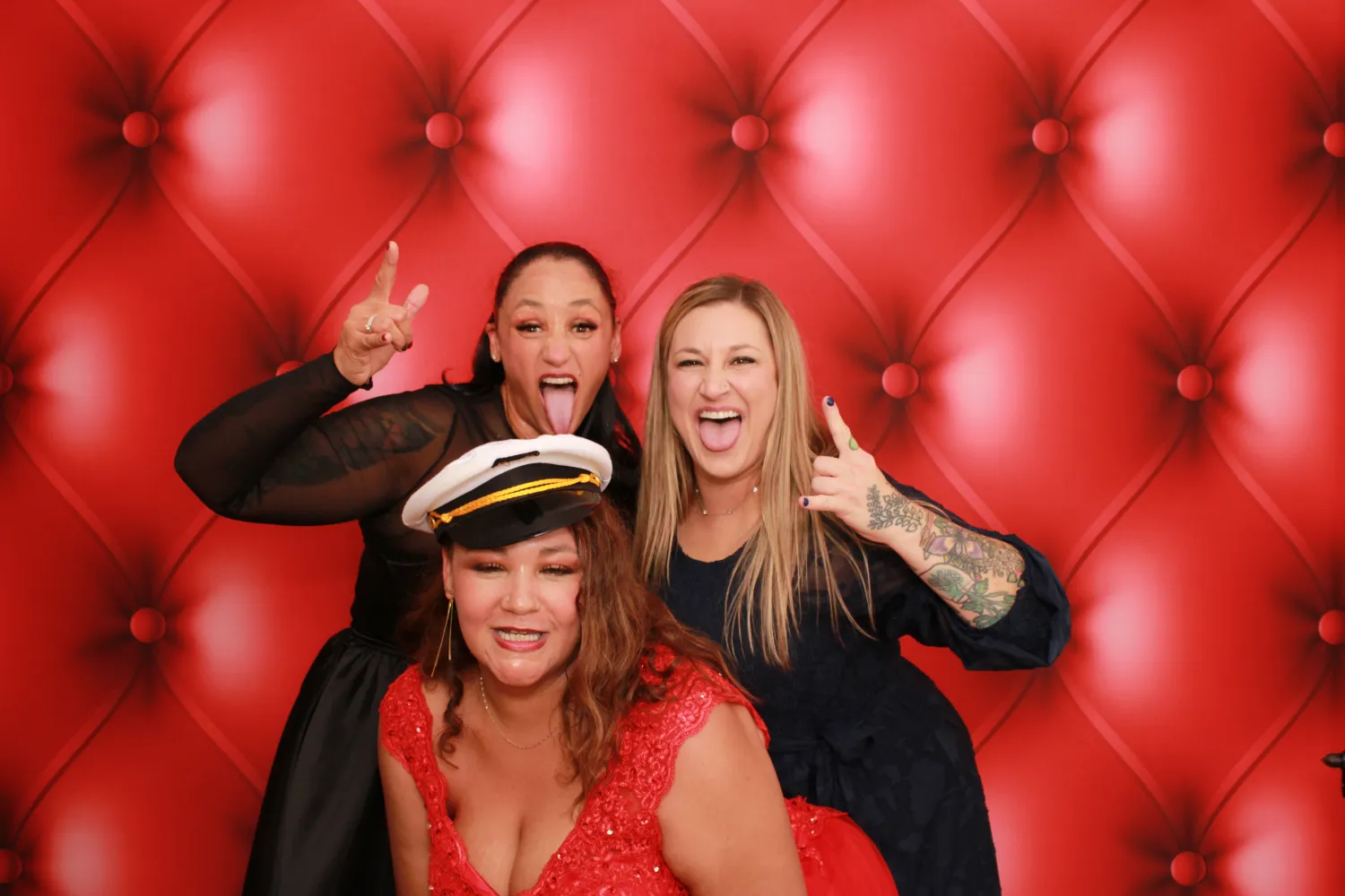 Three women posing playfully with silly faces against red tufted background
