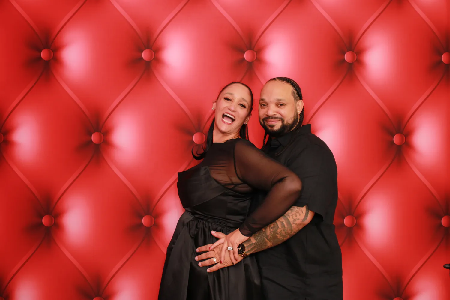 Joyful couple embracing in front of luxurious red tufted backdrop