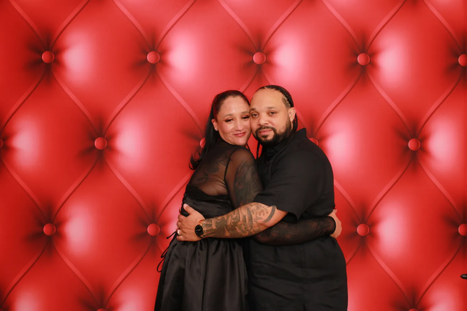 Couple in black embracing against a luxurious red tufted background