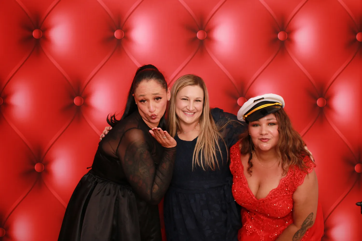 Three women posing playfully against a tufted red backdrop