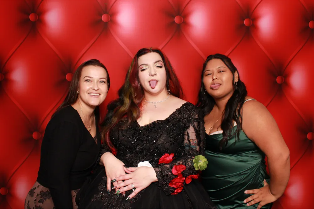 Three women posing together in front of red tufted background