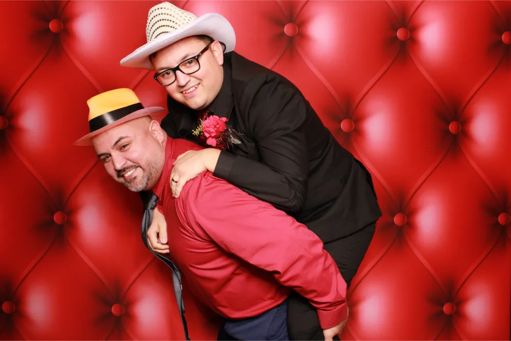 Two men in hats posing playfully in a red photo booth