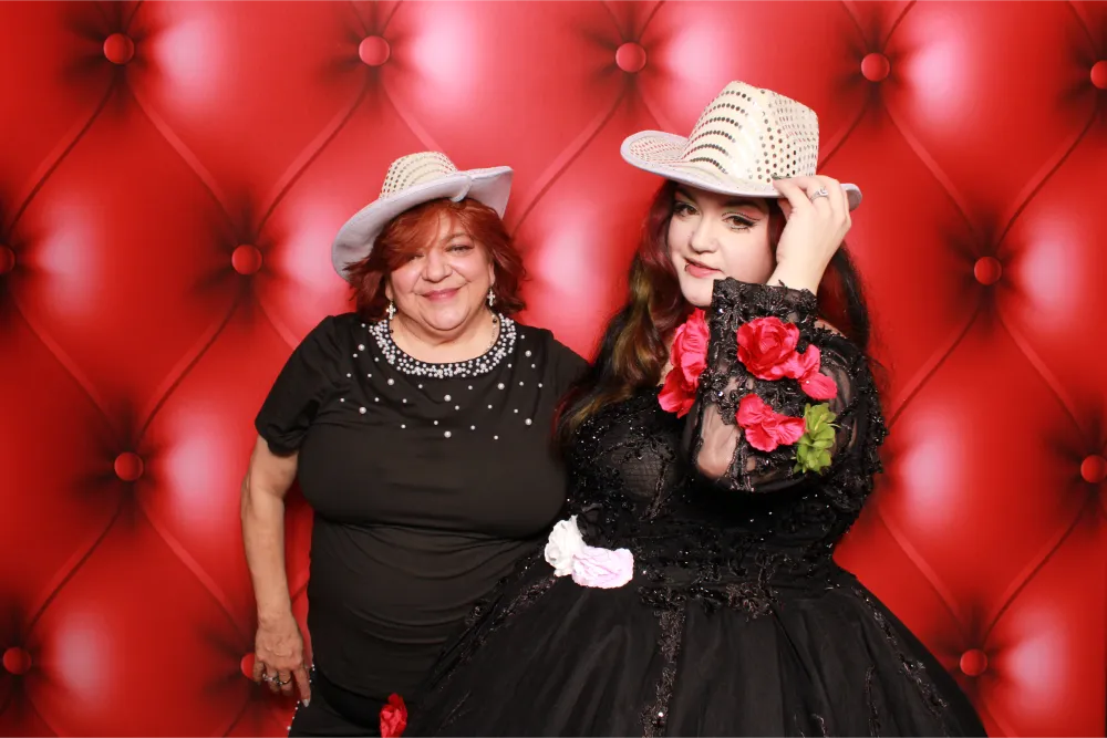 Two women in black dresses and cowboy hats pose against red backdrop