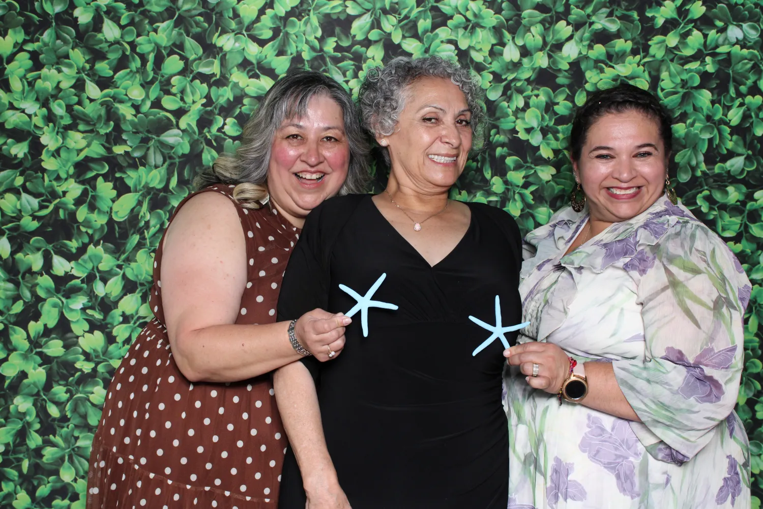 Three joyful women posing with starfish in front of green leaf backdrop