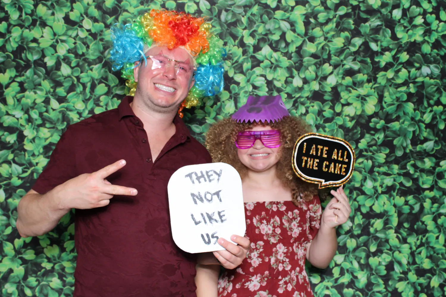 Two people in colorful wigs posing with funny signs in photo booth