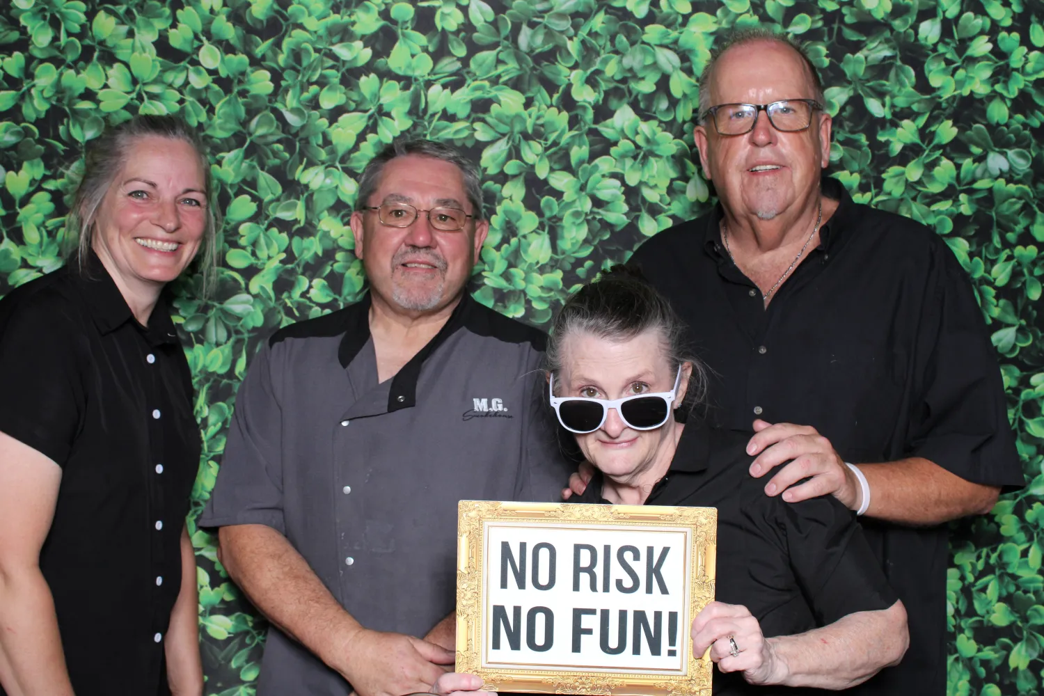 Four people pose with "No Risk No Fun" sign on green leafy background