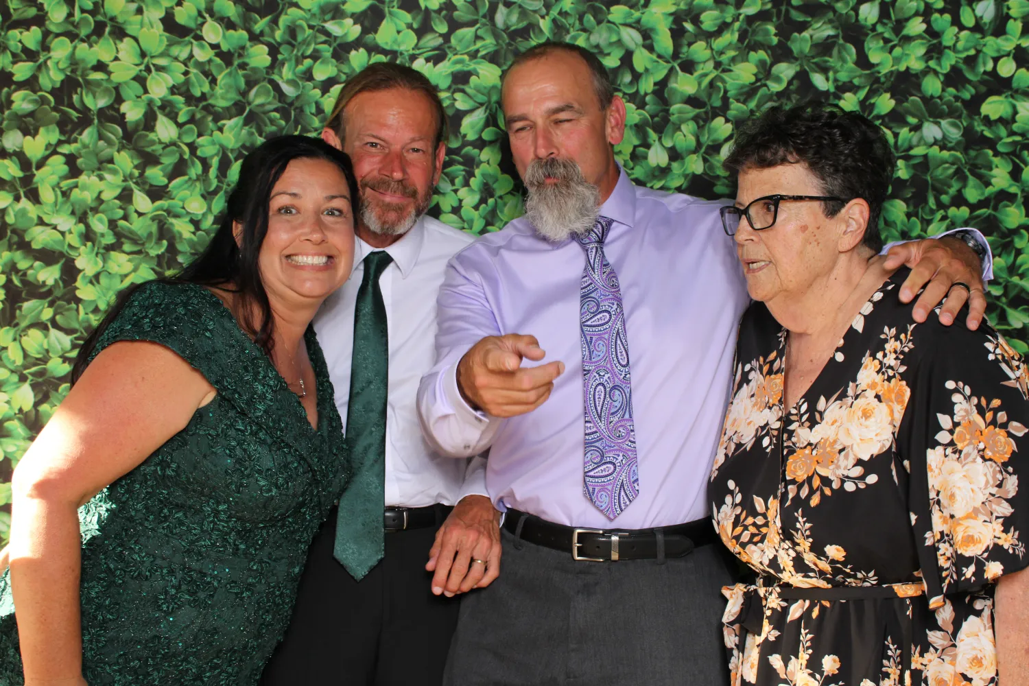 Four people posing together in front of green leafy background
