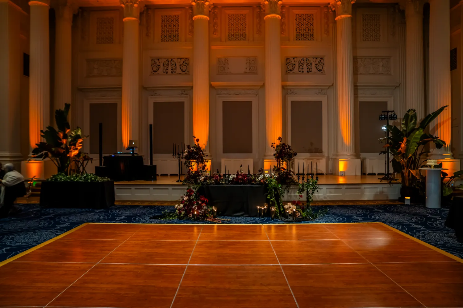 Elegant event space with wooden dance floor, floral arrangements, and warm lighting