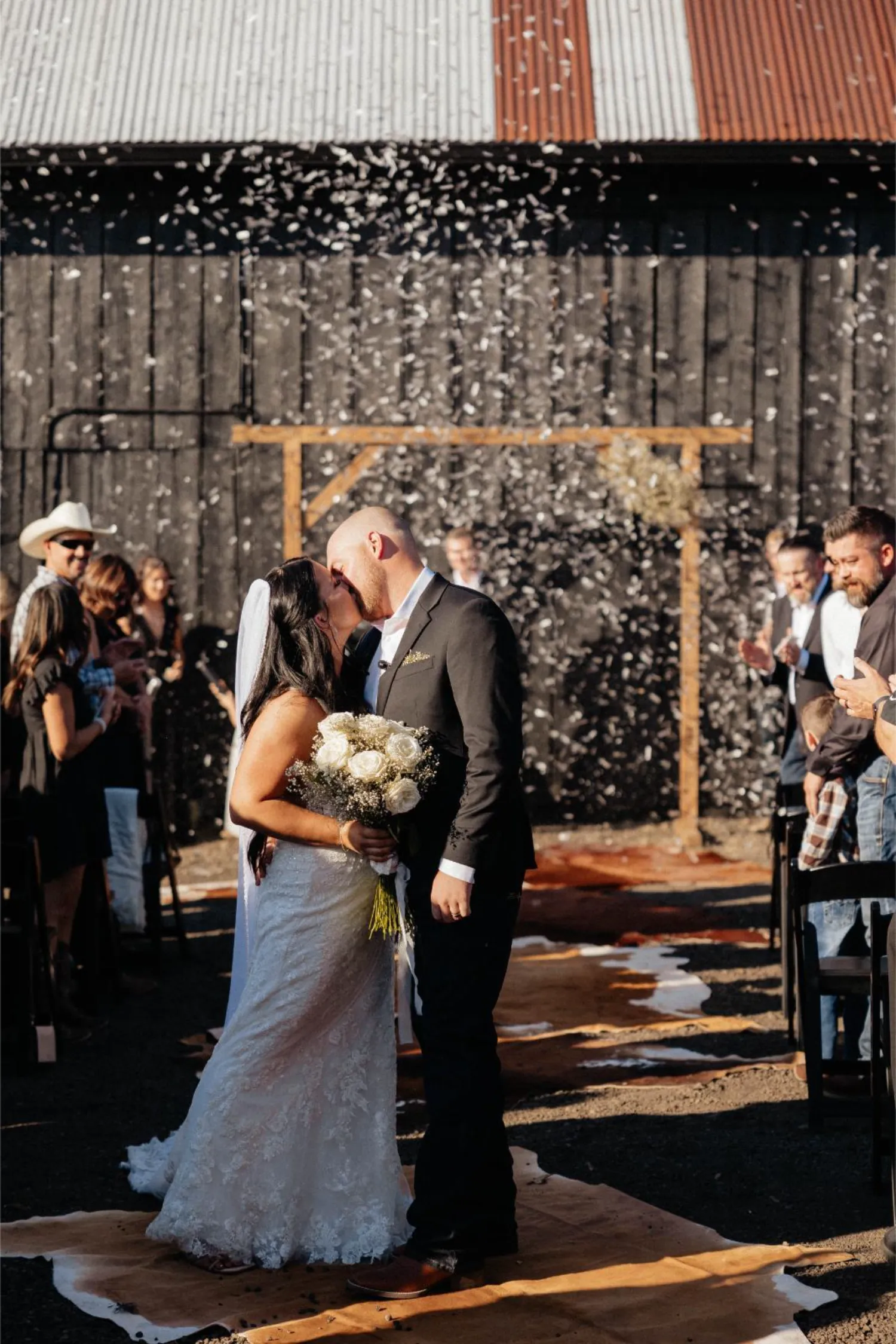 Wedding couple kissing under falling confetti at rustic barn venue