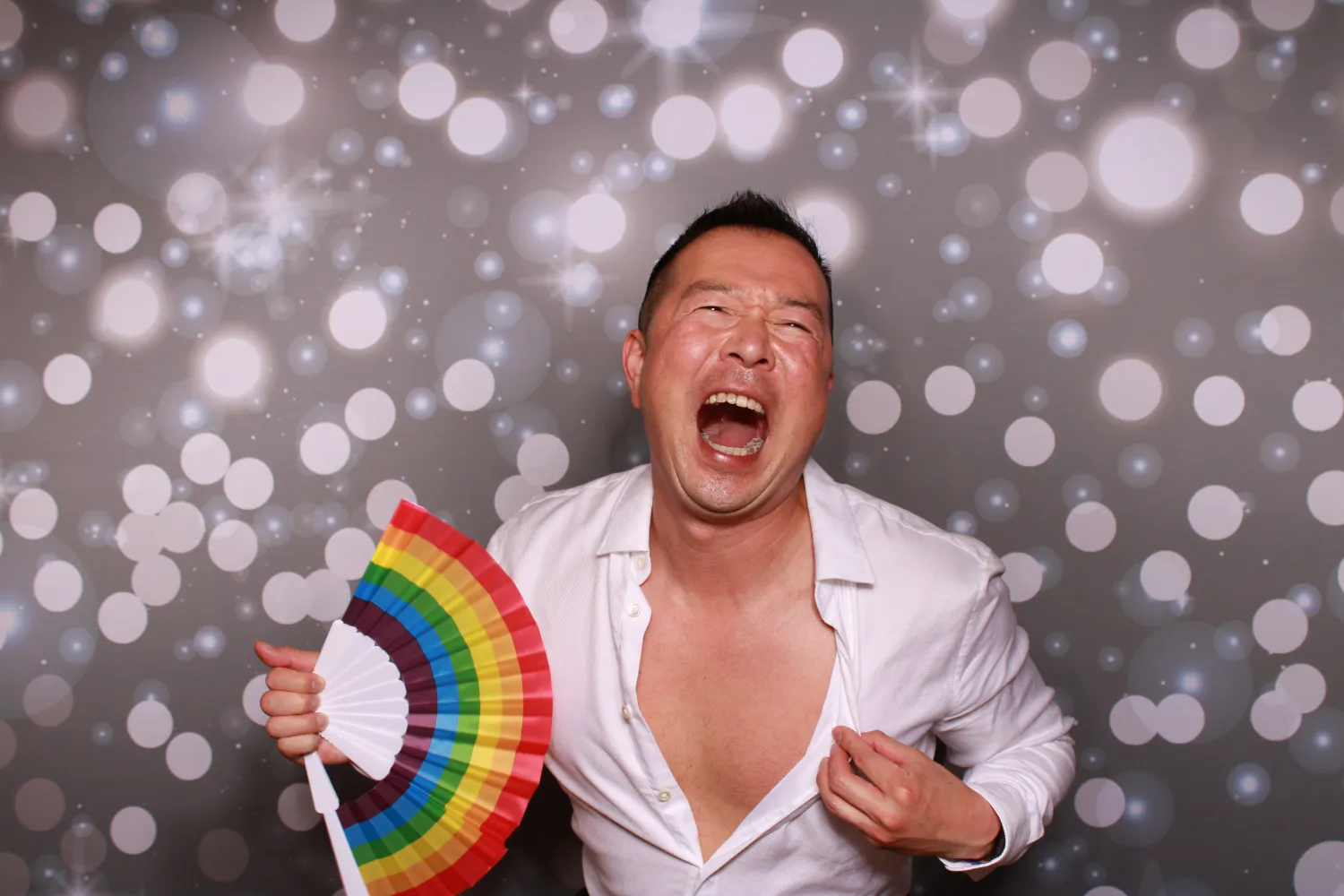 Joyful person with rainbow fan laughing against sparkly bokeh background