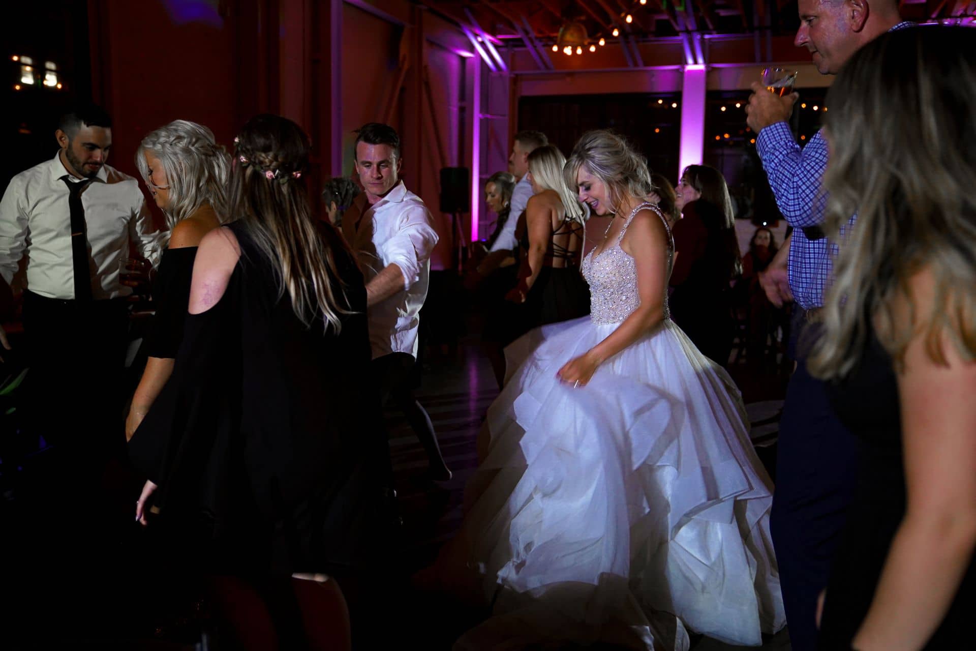 Bride in white wedding dress dancing at reception with purple lighting