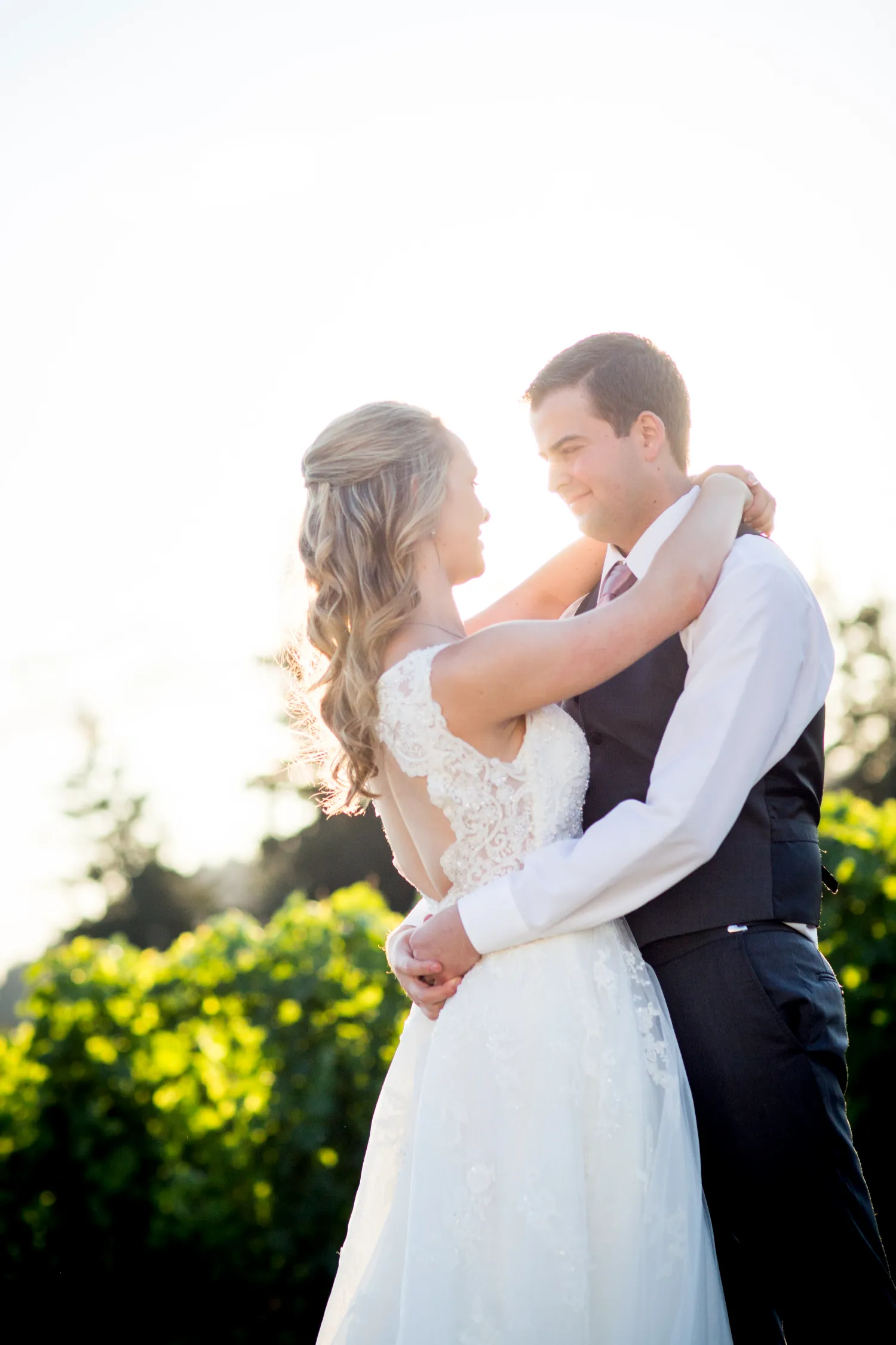 Romantic wedding photo of couple embracing in soft sunlight with greenery