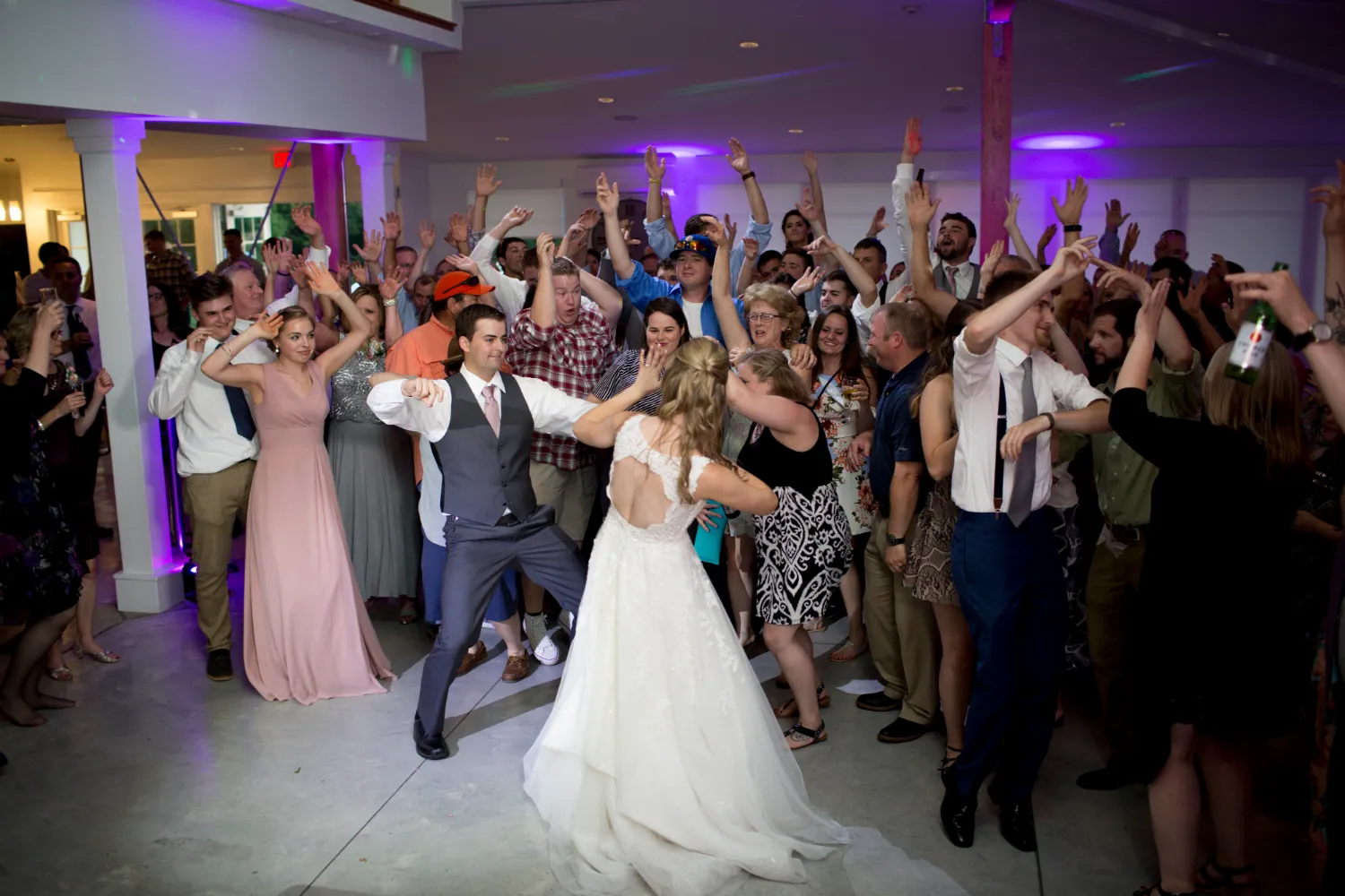 Wedding couple dancing with excited guests raising hands on dance floor
