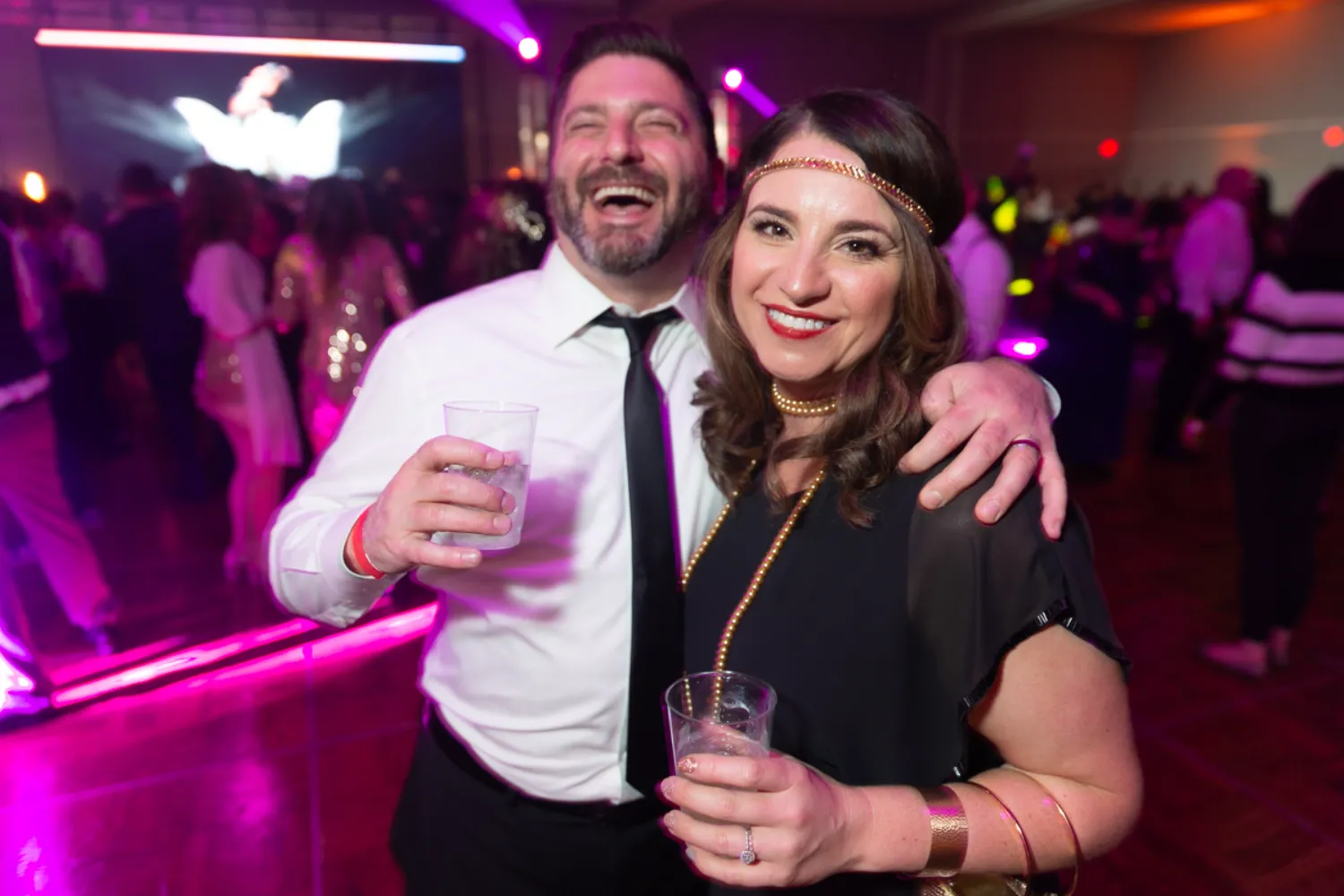 Two people laughing and enjoying a party with colorful purple lighting