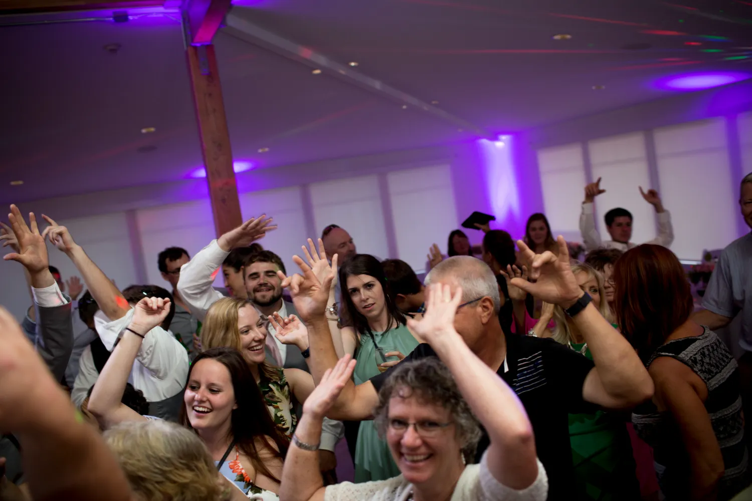 Crowded dance floor with people dancing and raising hands under purple lights