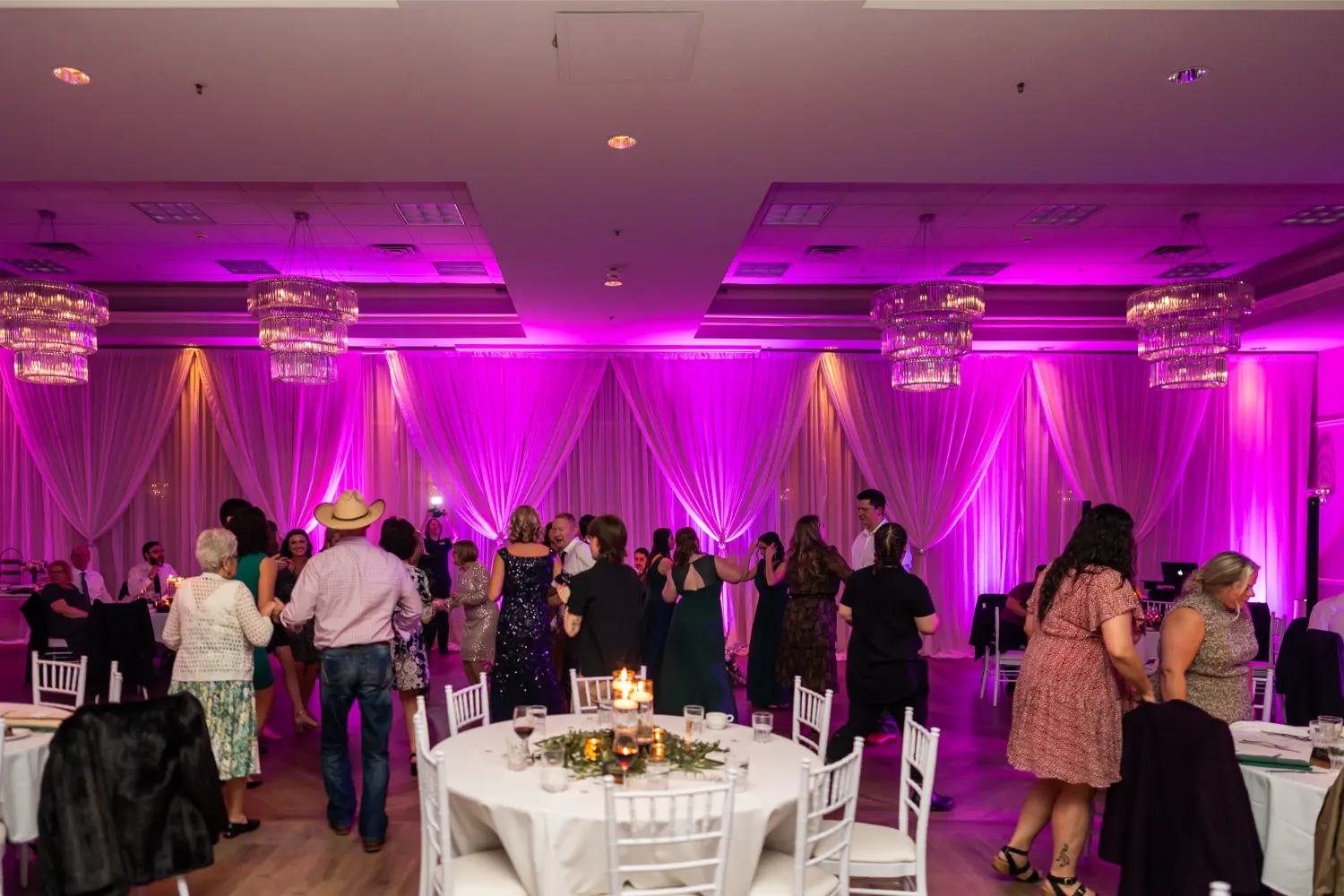 Elegant event with magenta-lit ballroom, guests dancing and socializing