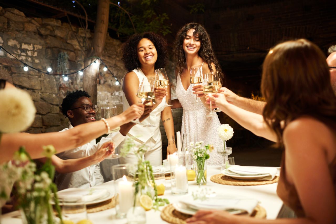 Friends toasting champagne glasses at candlelit dinner party with festive decor