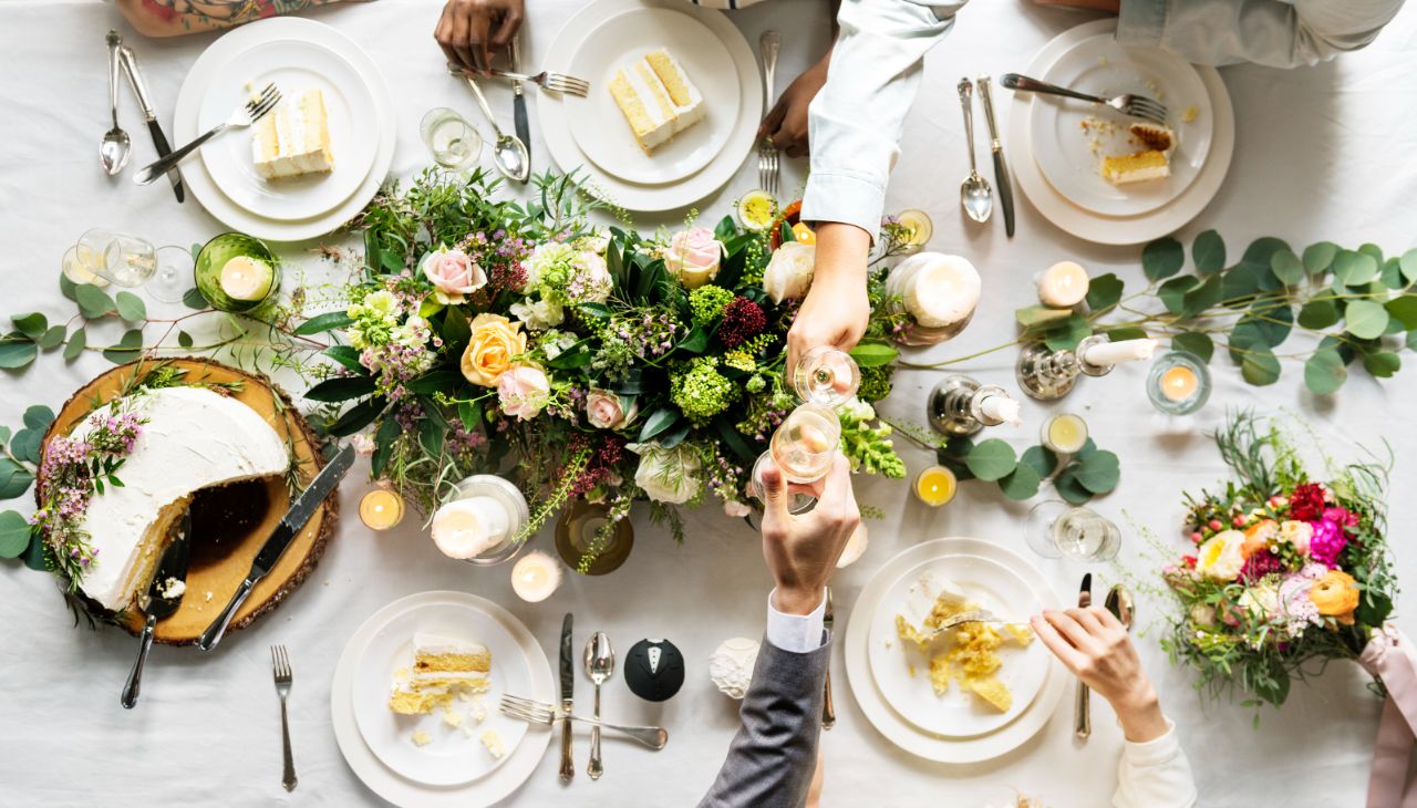 Elegant table setting with cake, floral centerpiece, candles, and dining hands