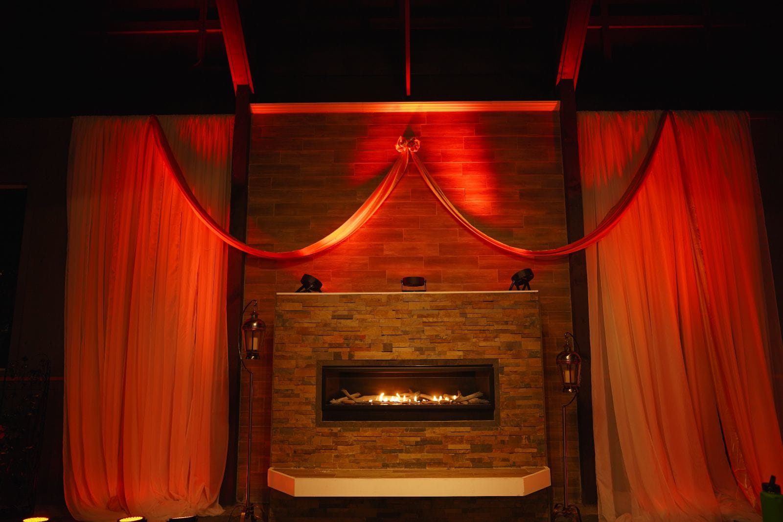 Dramatic red-lit fireplace with stone wall and elegant draped curtains