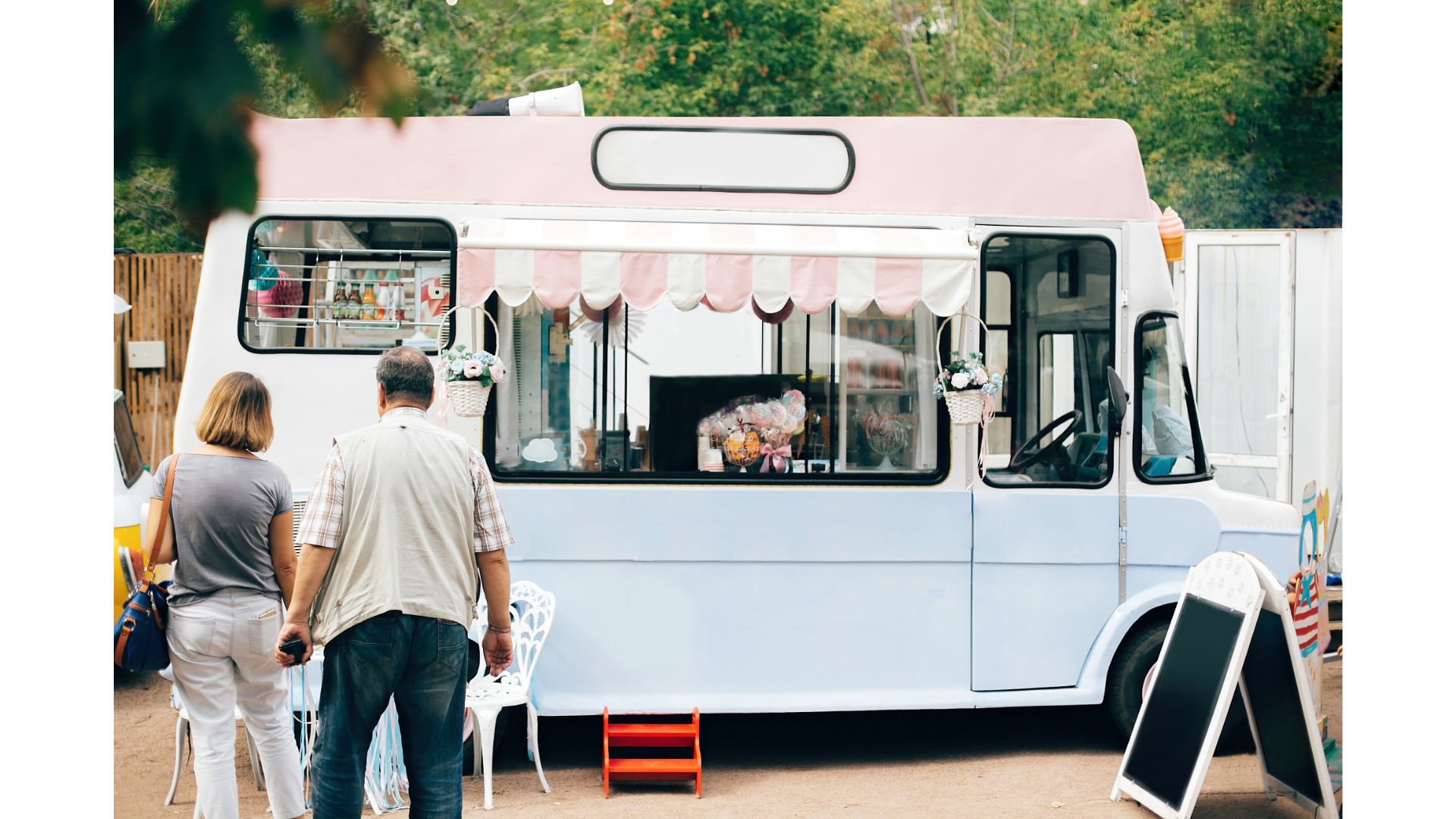 Two people ordering from a cute white vintage food truck with pink awning