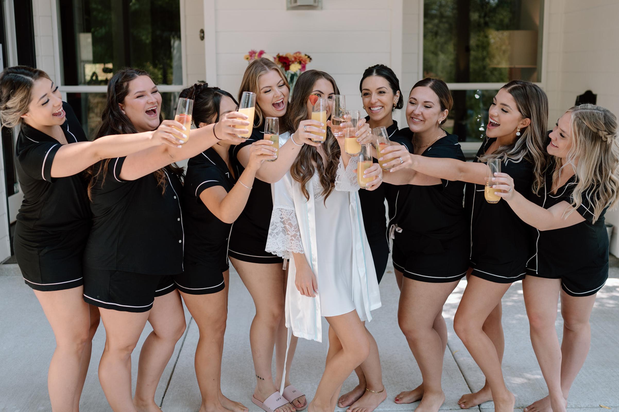 Bride and bridesmaids in matching black pajamas toasting with orange juice