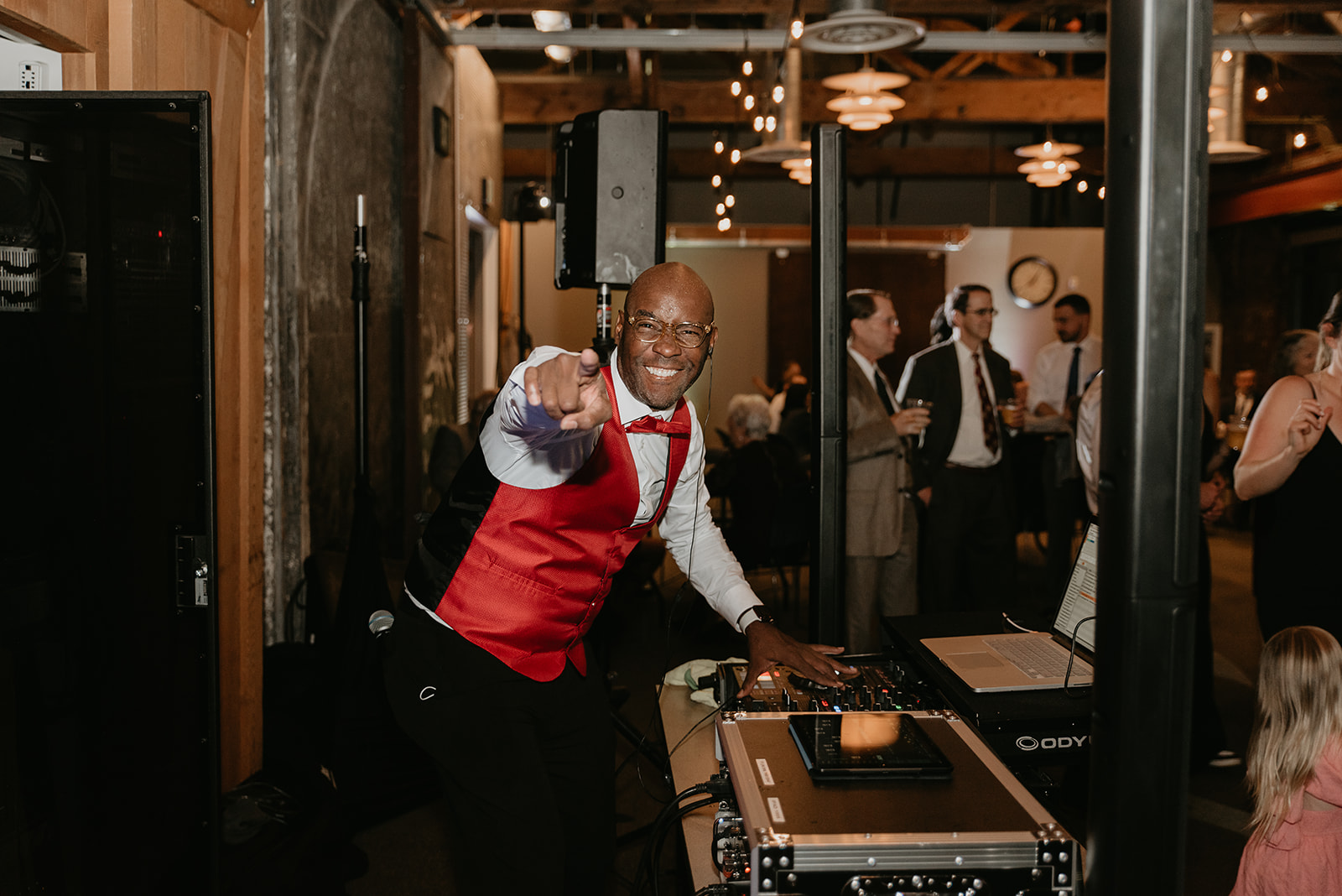 Excited DJ in red vest pointing and mixing music at wedding reception