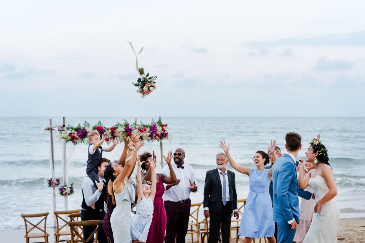 Joyful wedding party catching bouquet on sunny beach with ocean backdrop