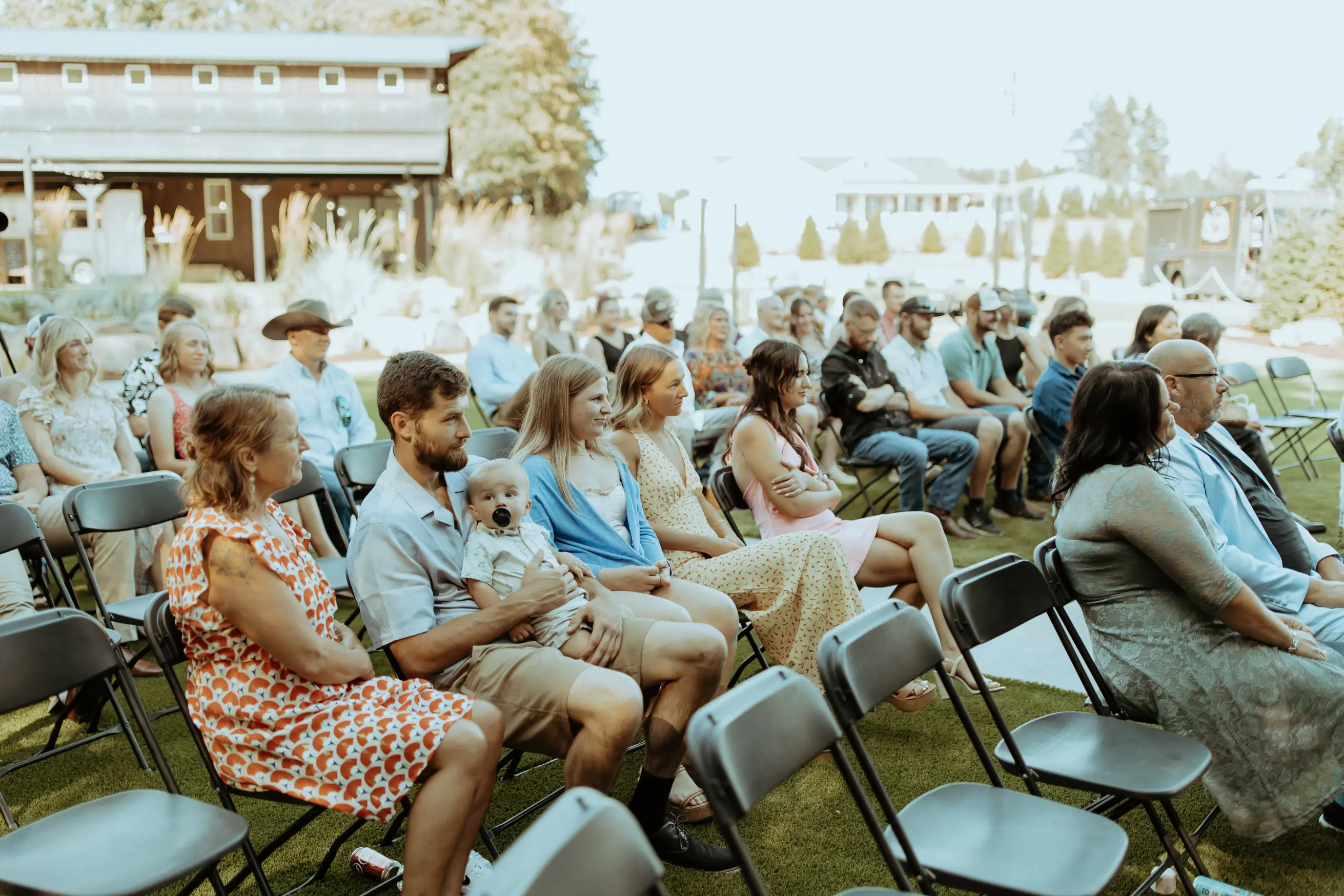 Wedding guests seated outdoors during a ceremony at Sage and Social wedding venue, with family and friends gathered on the lawn in front of the venue.